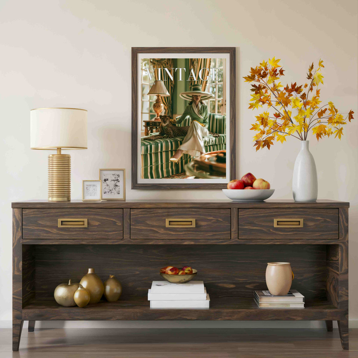 A dark brown wooden console table styled in a living room setting, featuring three drawers with brass handles, an open lower shelf, and decorative items including a lamp, framed art, books, and a white vase with autumn-colored leaves.