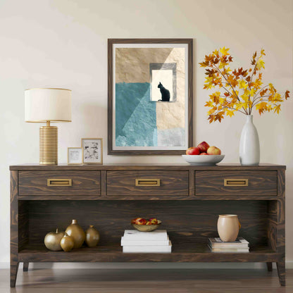 A dark brown wooden console table styled with a table lamp, framed art, a white vase with autumn leaves, fruit, and decorative objects against a neutral beige wall.