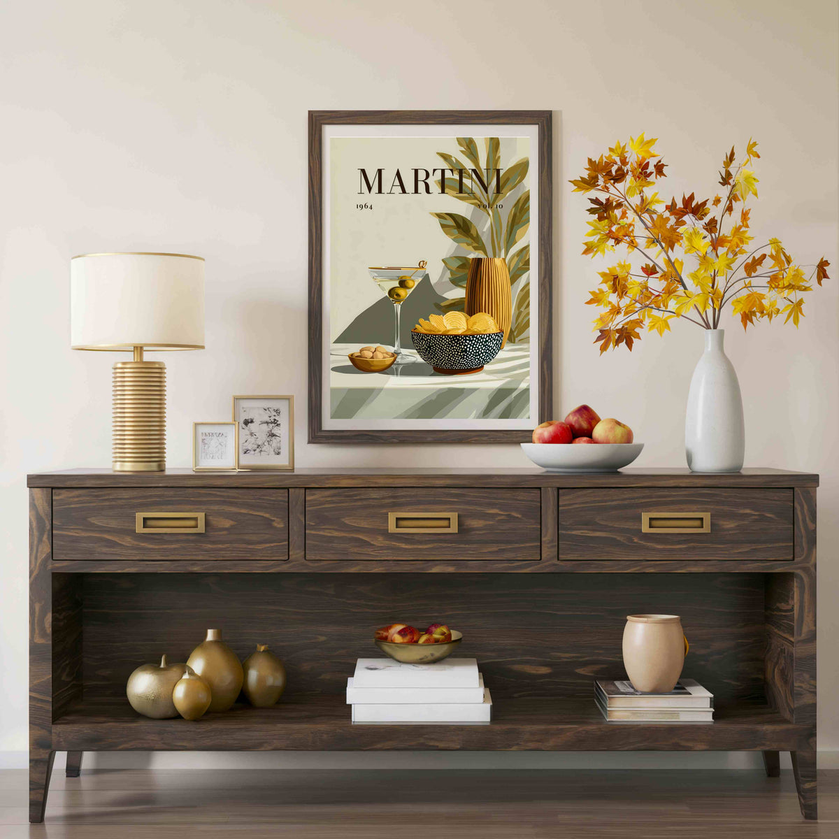A dark brown wooden console table styled in a living room setting, decorated with a table lamp, small frames, books, decorative gourds, a bowl of fruit, and a white vase with autumn-colored leaves. Above the console is a framed art print with the text 'MARTINI 1964'.