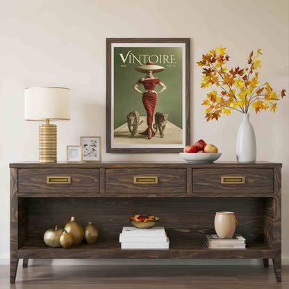 A dark wood console table styled in a living room setting, featuring a framed vintage 'Vintoire' poster, a table lamp, a white vase with autumn leaves, and decorative accents on top and in the open shelf below.