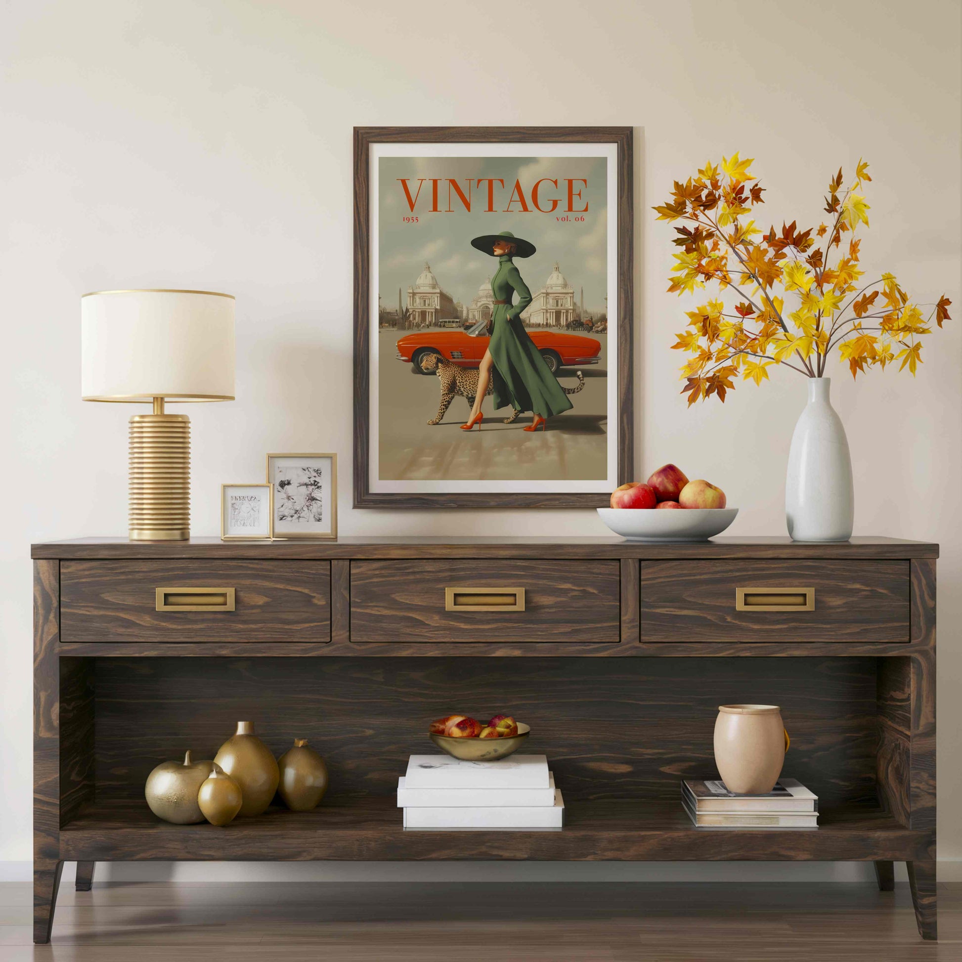 A dark wood console table styled in a living room setting, featuring a vintage 'Vintage' art print on the wall above it, a table lamp, small picture frames, a bowl of apples, and a vase with autumn leaves.