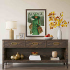 A framed vintage-style magazine cover print hangs on a beige wall above a dark wood console table. The print shows a woman in a green coat and hat holding a leopard cub, with the word 'VINTAGE' at the top.