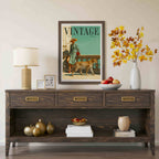 A framed vintage-style magazine cover print hangs on a beige wall above a dark wood console table. The print shows a woman walking a cheetah with the word 'VINTAGE' at the top.