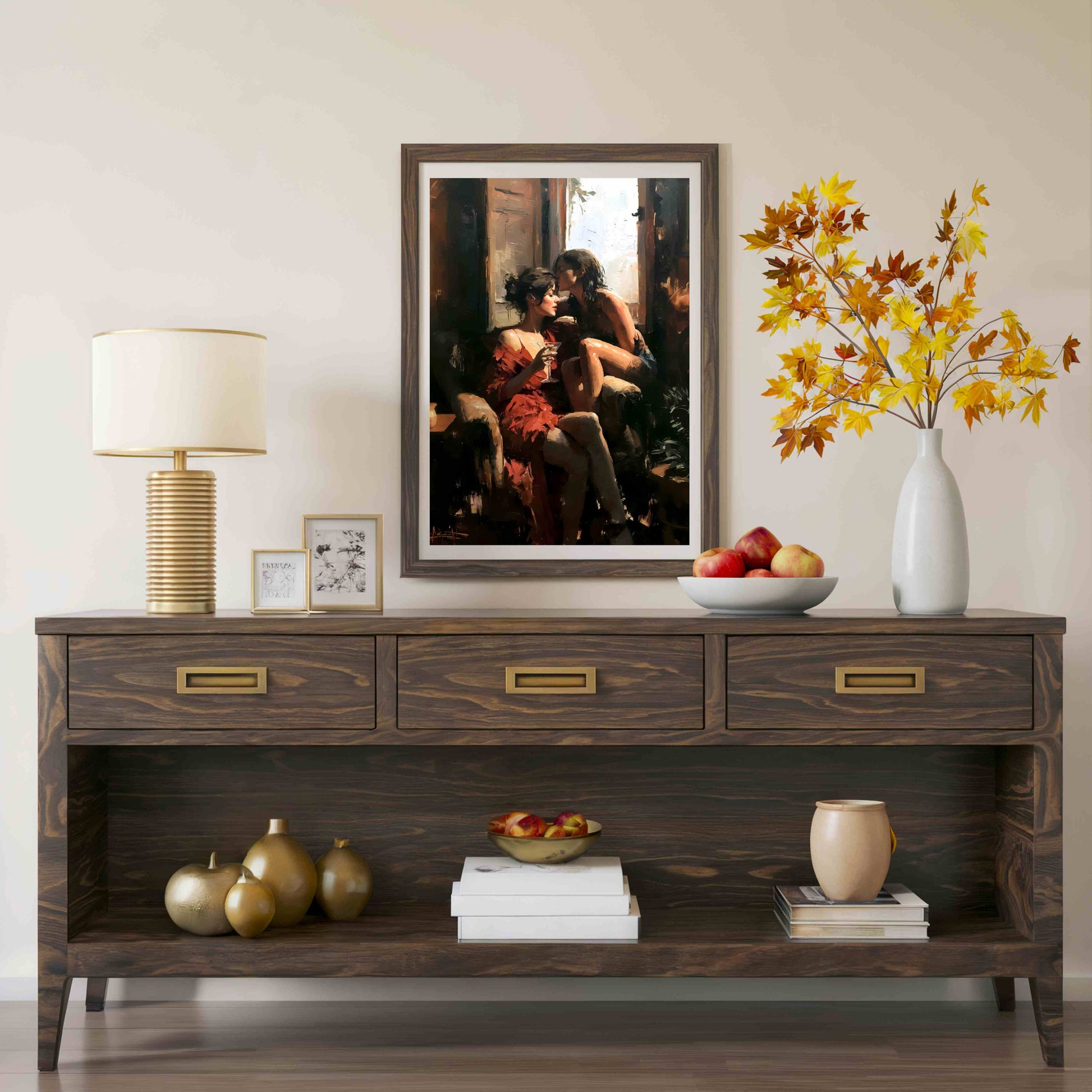 A dark brown wooden console table styled in a living room setting, featuring a large framed art print of a couple on the wall above it. The table is decorated with a lamp, small frames, a bowl of apples, a vase with autumn leaves, and decorative gourds.
