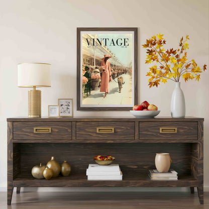 A dark brown wooden console table styled in a living room setting, featuring a vintage 'Vintage' magazine poster hanging above it, a table lamp, decorative vases, and fruit bowls.