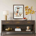A dark brown wooden console table styled in a living room setting, featuring a vintage 'Vintage Vogue' magazine cover hanging on the wall above it, a table lamp, decorative vases, and fruit bowls.