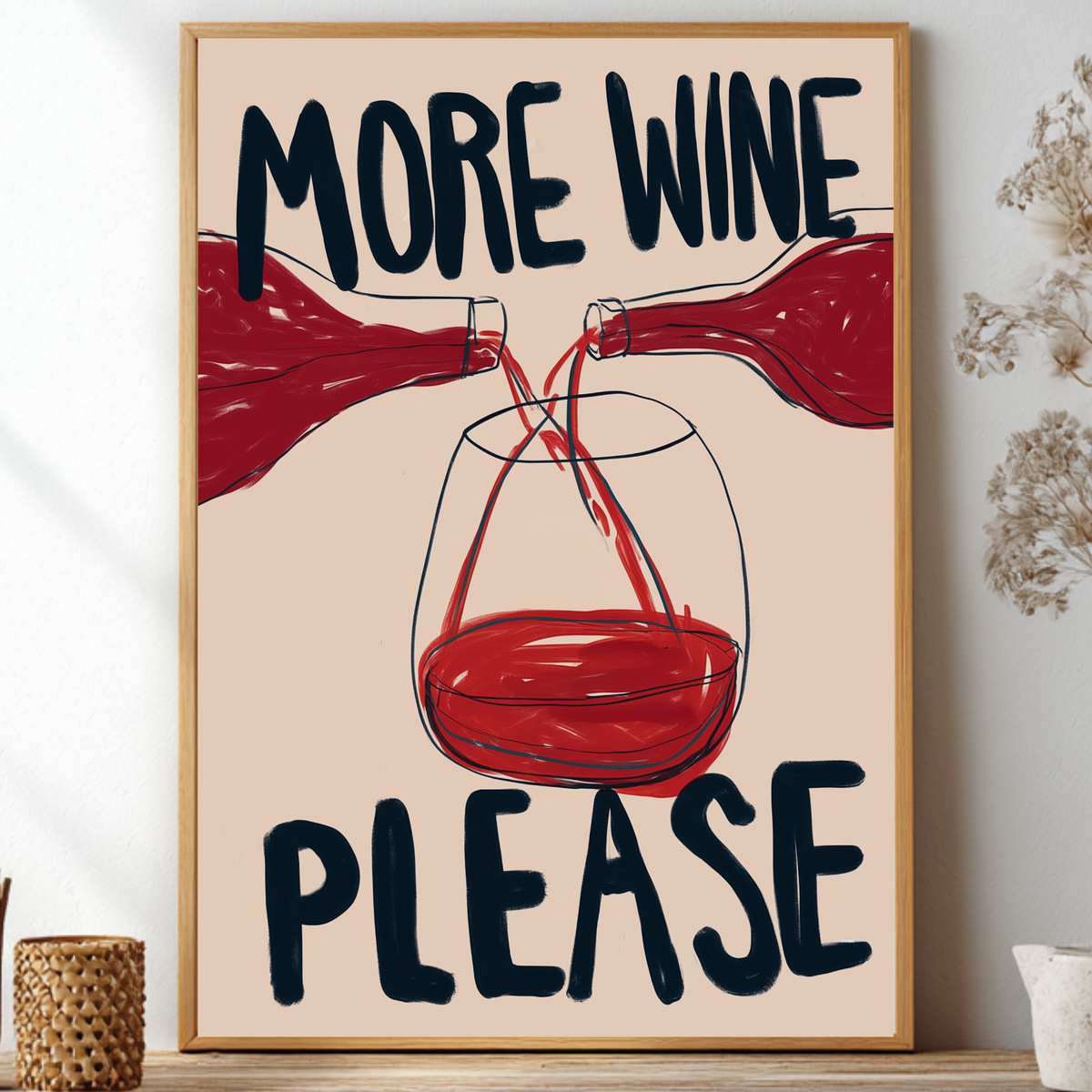 A framed wall art print with the text 'MORE WINE PLEASE' and an illustration of red wine bottles pouring into a glass, displayed on a shelf in a styled interior setting.