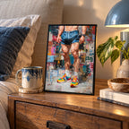 Newsprint framed print on a wooden bedside table beside a lamp, a mug, a plant and books, showing a man's legs in blue shorts and colourful trainers.