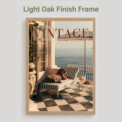 A framed art print featuring a vintage-style coastal balcony scene with a striped chaise lounge, checkered floor, and large 'VINTAGE' text across the top, shown against a light gray background with the text 'Light Oak Finish Frame' above it.