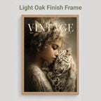 A framed art print featuring a vintage-style portrait of a woman cradling a spotted cat, with the text 'VINTAGE' across the top. The frame is light oak wood, shown against a light gray background with the text 'Light Oak Finish Frame' above it.