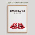 A framed personalized art print with a light oak finish frame, featuring the text 'EMMA & SARAH 12 JUNE 2026' above a pair of red lips with white polka dots, shown against a light gray background with the text 'Light Oak Finish Frame' at the top.