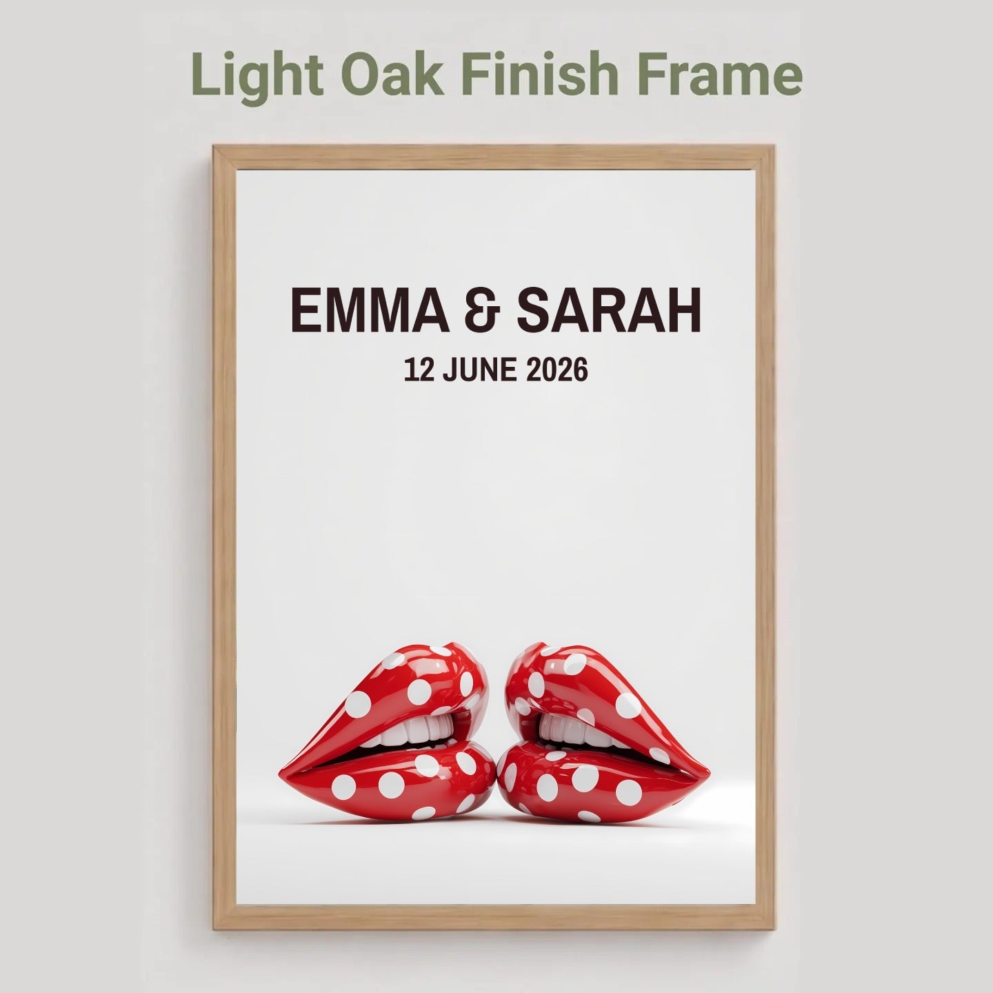 A framed personalized art print with a light oak finish frame, featuring the text 'EMMA & SARAH 12 JUNE 2026' above a pair of red lips with white polka dots, shown against a light gray background with the text 'Light Oak Finish Frame' at the top.