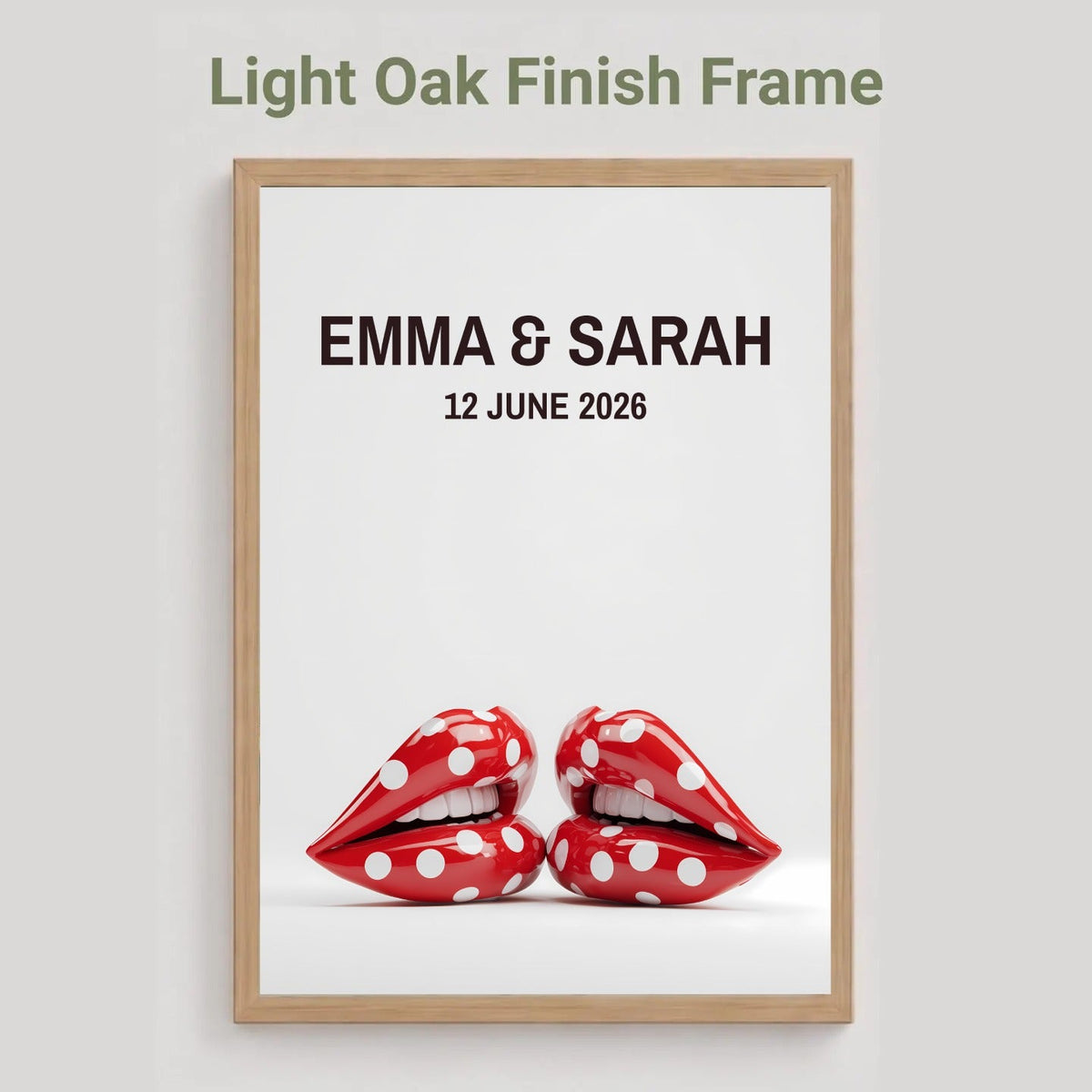 A framed personalized art print with a light oak finish frame, featuring the text 'EMMA & SARAH 12 JUNE 2026' above a pair of red lips with white polka dots, shown against a light gray background with the text 'Light Oak Finish Frame' at the top.