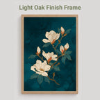 A framed floral art print featuring white magnolia blossoms on a dark teal marbled background, shown in a light oak finish frame against a light gray wall. Text above reads 'Light Oak Finish Frame'.