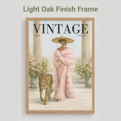 A framed art print featuring a vintage magazine cover illustration with the word VINTAGE at the top, shown against a light gray background. The print depicts a woman in a pink fur coat and hat walking a leopard, enclosed in a light oak finish frame.