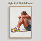 Rest gay art print in the light oak finish frame option, a seated man resting his head on his knees in colourful trainers, labelled Light Oak Finish Frame
