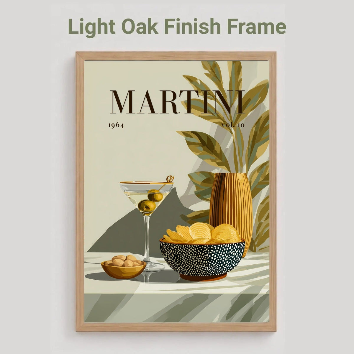 A framed art print featuring a retro Martini cocktail illustration with olive olives, a yellow martini glass, a patterned bowl of chips, and a striped vase with leaves. The print is housed in a light oak finish frame, shown against a neutral gray background with the text 'Light Oak Finish Frame' above it.