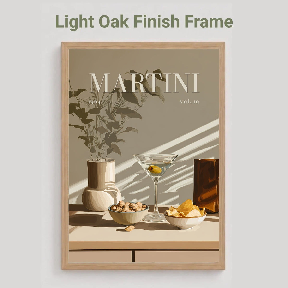 A framed art print with a light oak finish frame, featuring a minimalist still life illustration of a martini glass, bowls of snacks, and a vase with leaves. The text 'MARTINI vol.