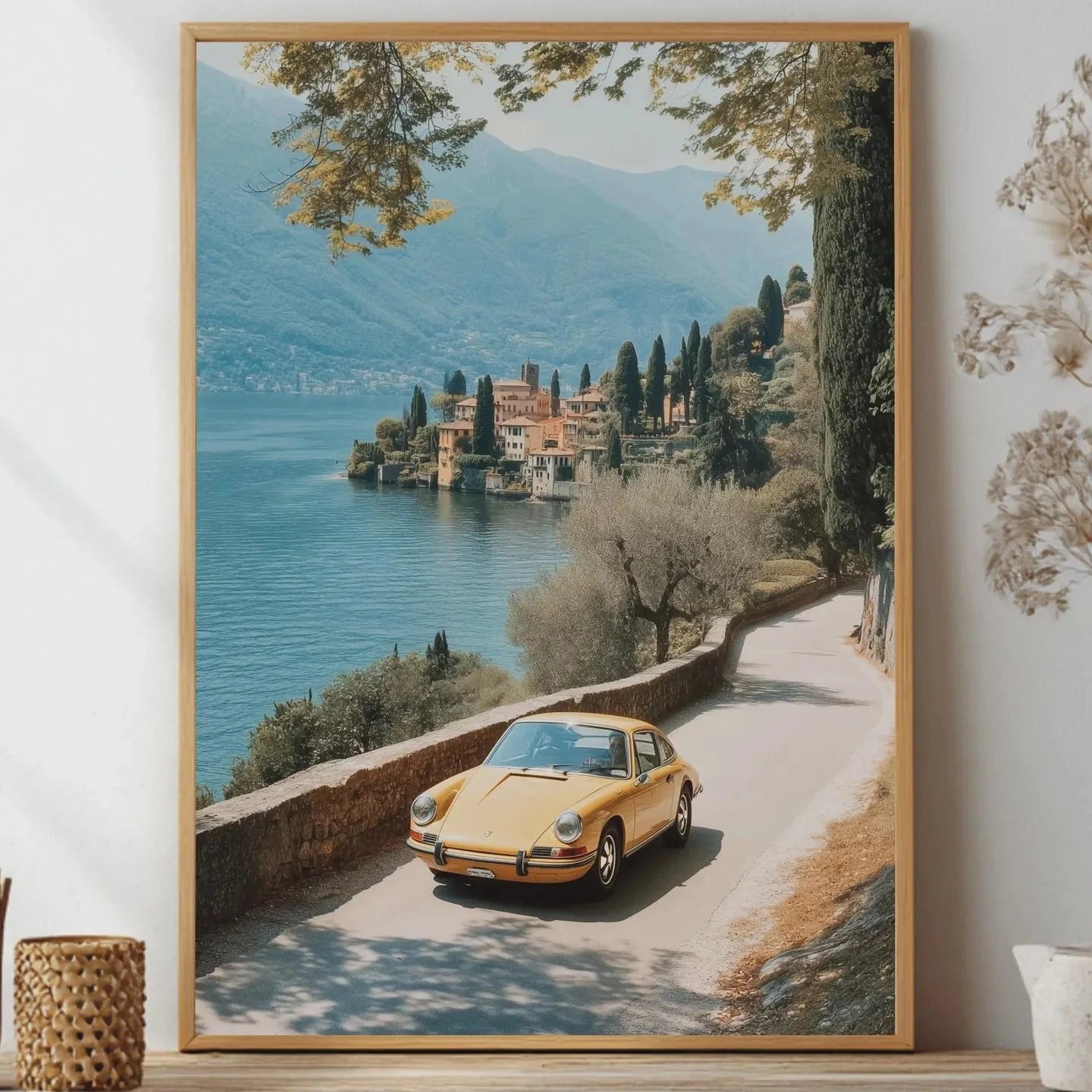 Framed artwork of a scenic view with a yellow porsche car by a lake, placed on a shelf.