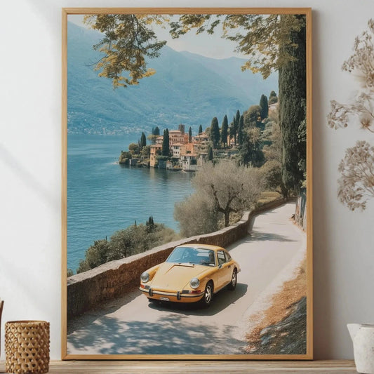 Framed artwork of a scenic view with a yellow porsche car by a lake, placed on a shelf.