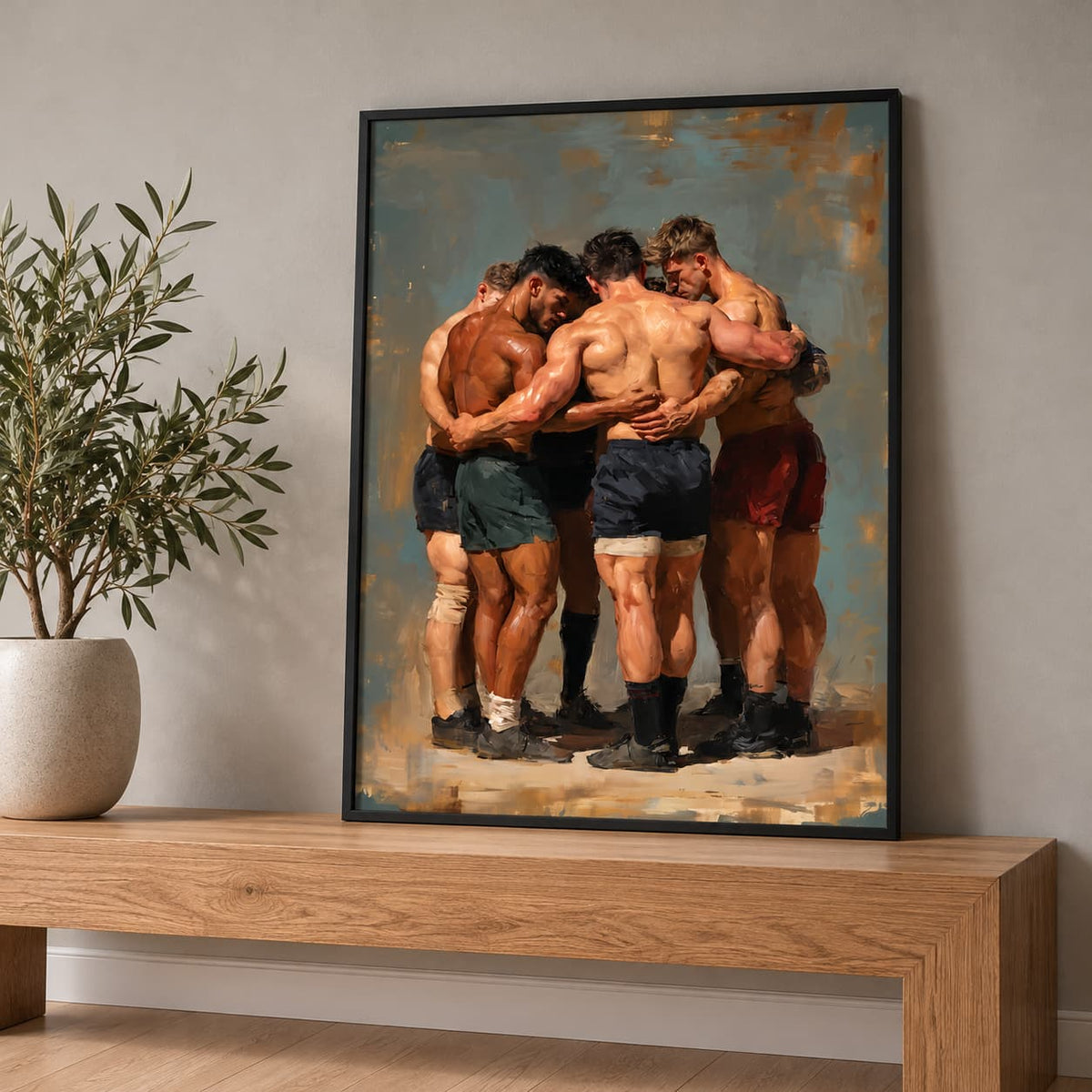 A framed art print depicting five rugby players hugging, displayed on a wooden console table next to a potted plant against a neutral gray wall.
