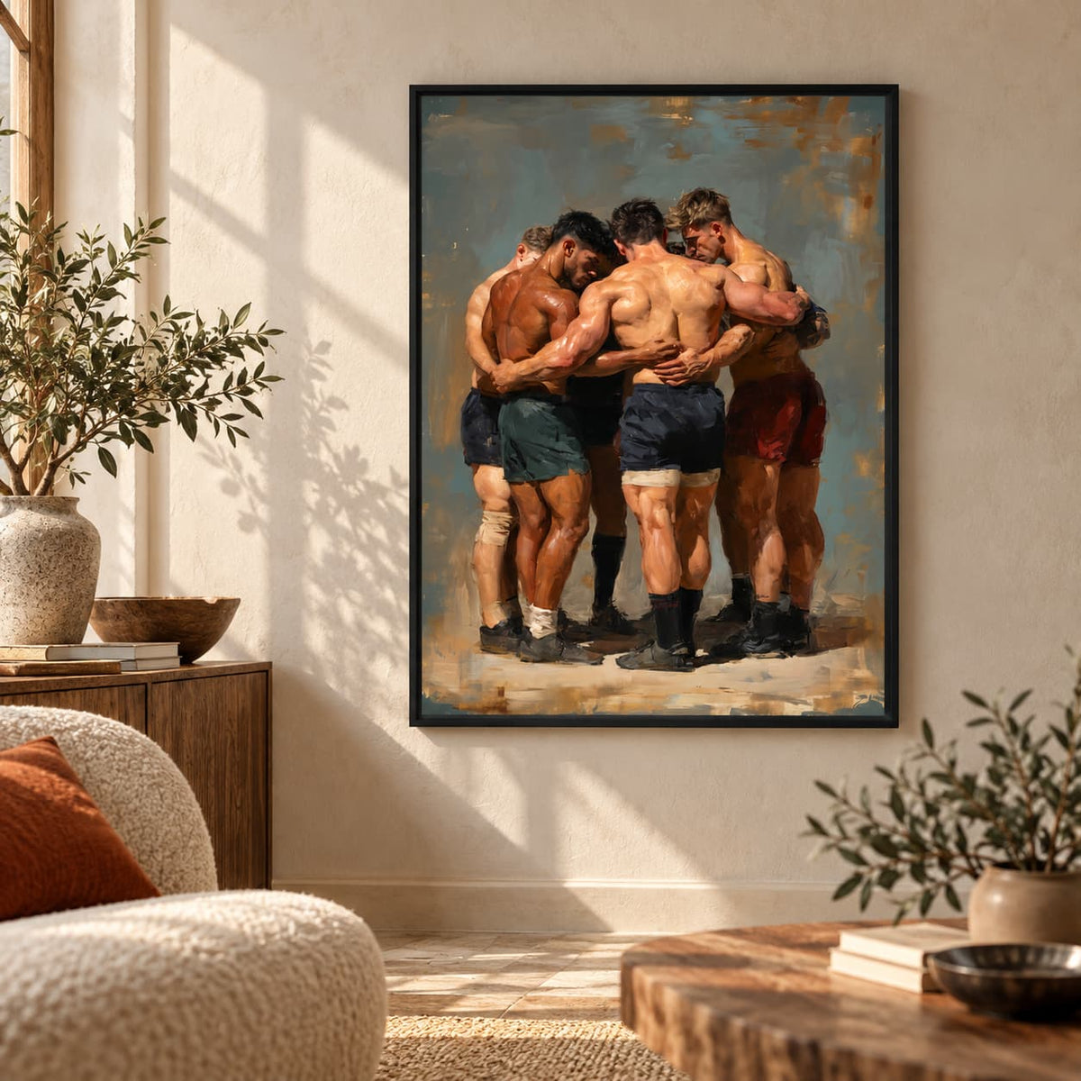 A framed art print depicting four muscular men hugging, displayed on a beige wall in a modern living room setting with a sofa, plants, and wooden furniture.