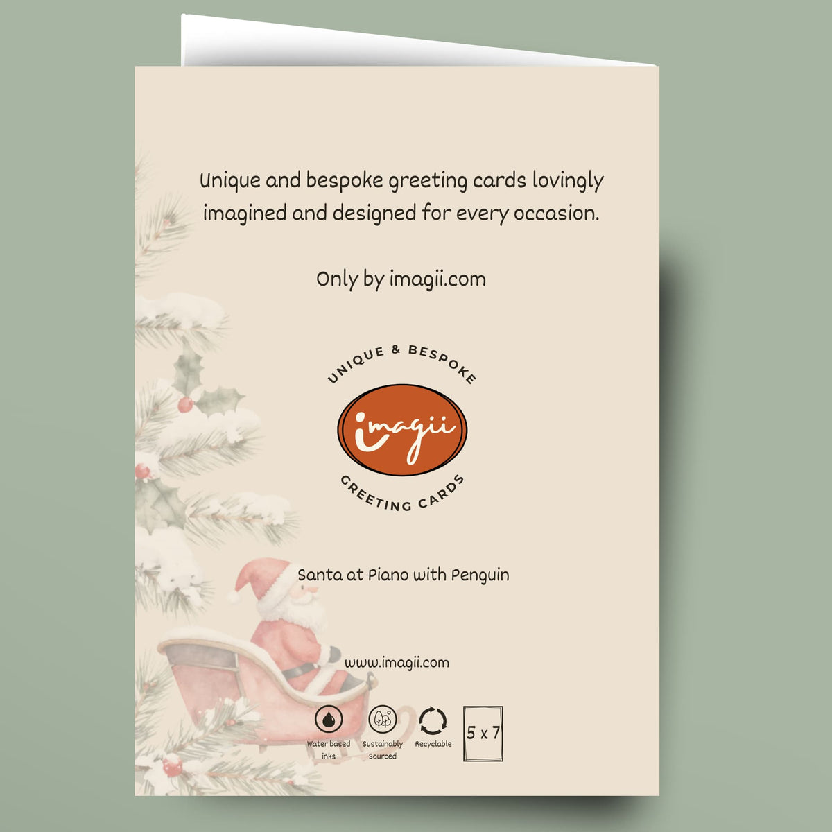 A single greeting card shown flat against a muted sage green background. The card has a cream front with printed holiday illustrations along the left side, including pine branches, holly, and a pink sleigh.