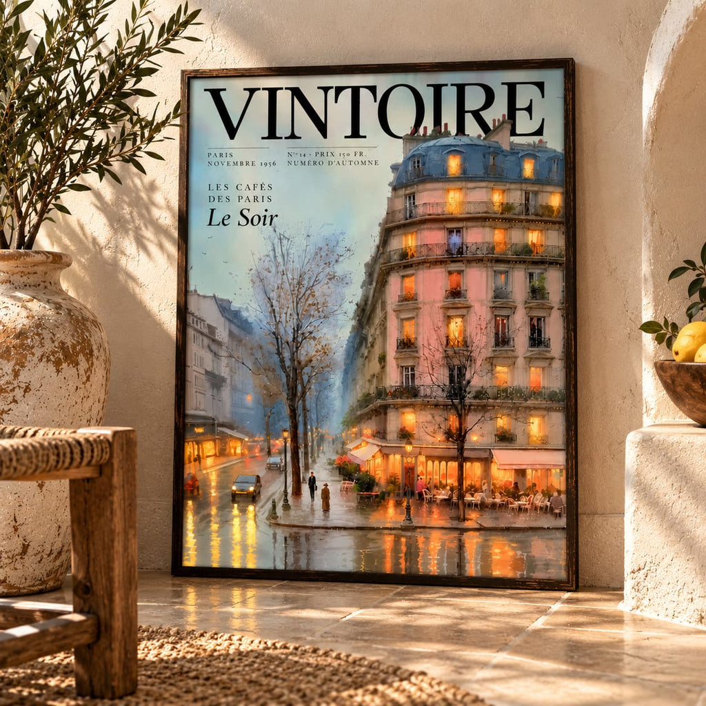 A framed vintage-style poster leaning against a textured cream wall in a sunlit interior. The poster reads "VINTOIRE" and shows a Parisian street scene with a lit café building, trees, and warm reflections on wet pavement.