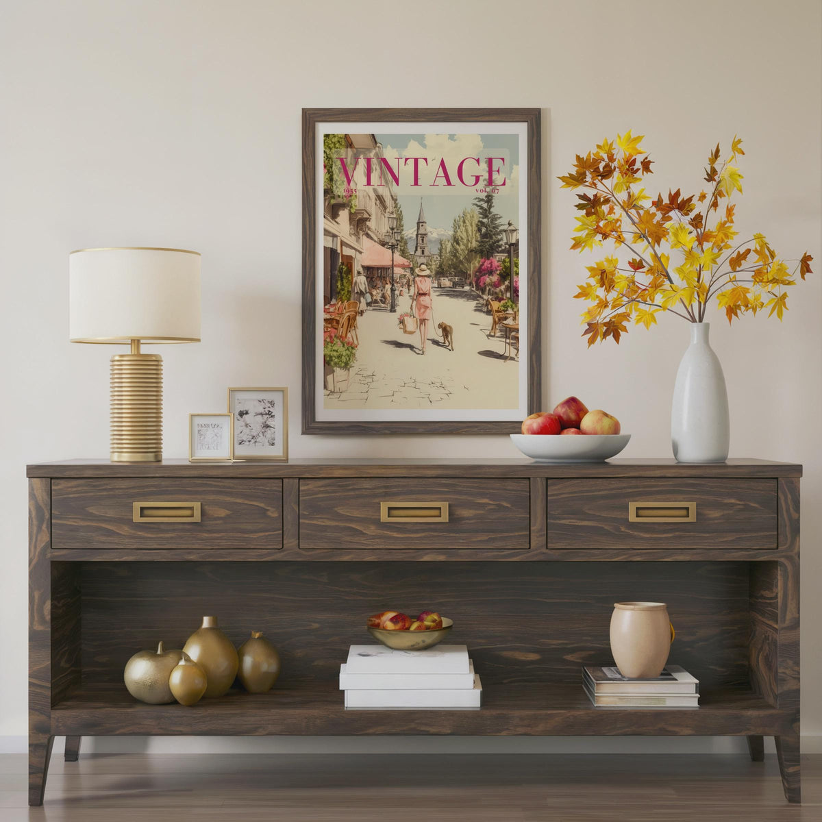 A framed vintage-style art print with the word 'VINTAGE' hangs on a beige wall above a dark wood console table styled with a lamp, small frames, a vase of autumn leaves, and decorative objects.