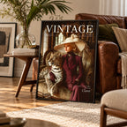 A framed vintage-style poster leaning against a brown leather sofa in a living room. The poster features the word 'VINTAGE' at the top and an illustration of a woman in a wide-brimmed hat and dark red coat sitting beside a spotted leopard.