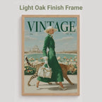 A framed vintage-style poster or magazine cover featuring a woman in a green dress walking with a leopard, with the word VINTAGE at the top. The frame is light oak wood, and the image is shown against a light gray background with the text 'Light Oak Finish Frame' above.