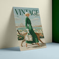 A vintage-style illustrated poster or print leaning against a wall on a light blue surface. The artwork shows a woman in a long green dress walking with two cheetahs near water and flowers, with the large word 'VINTAGE' across the top.