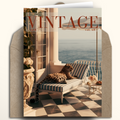 A vintage-style greeting card featuring a luxurious balcony scene with a leopard lounging on a striped chaise lounge by the sea, shown with a kraft envelope behind it. The card prominently displays the word 'VINTAGE' at the top.