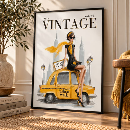 A framed vintage-style fashion poster leaning against a wall in a styled interior. The poster shows a woman in a black outfit with a yellow scarf sitting on a yellow taxi, with the text '1955 VINTAGE vol.