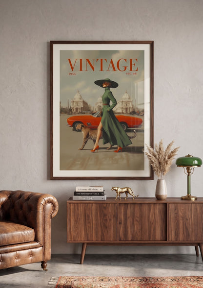 A framed vintage-style poster hangs on a light gray wall above a wooden sideboard in a styled room. The poster features the word 'VINTAGE' at the top, an orange car, a woman in a long green dress and black hat, and a dog.