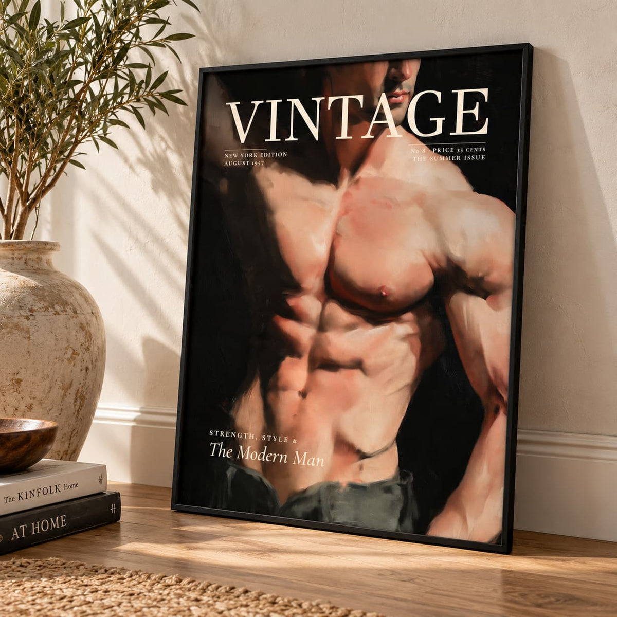 A framed vintage-style poster leaning against a wall on a wooden floor, showing a muscular male torso with the large word VINTAGE at the top. The room includes a vase with leaves, stacked books, and a rug.