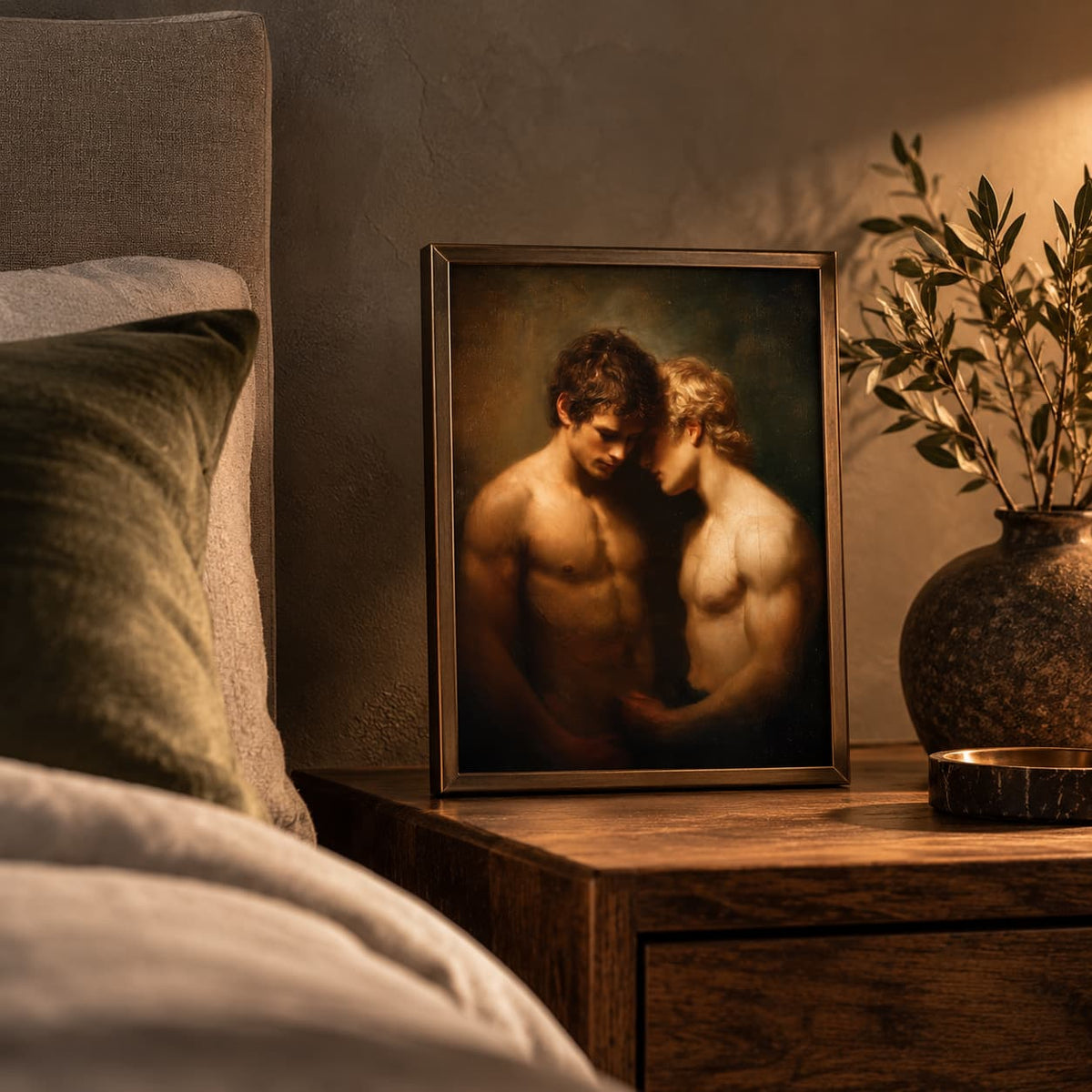 A framed art print depicting two shirtless men embracing, displayed on a wooden nightstand in a warmly lit bedroom next to a bed and a potted plant.