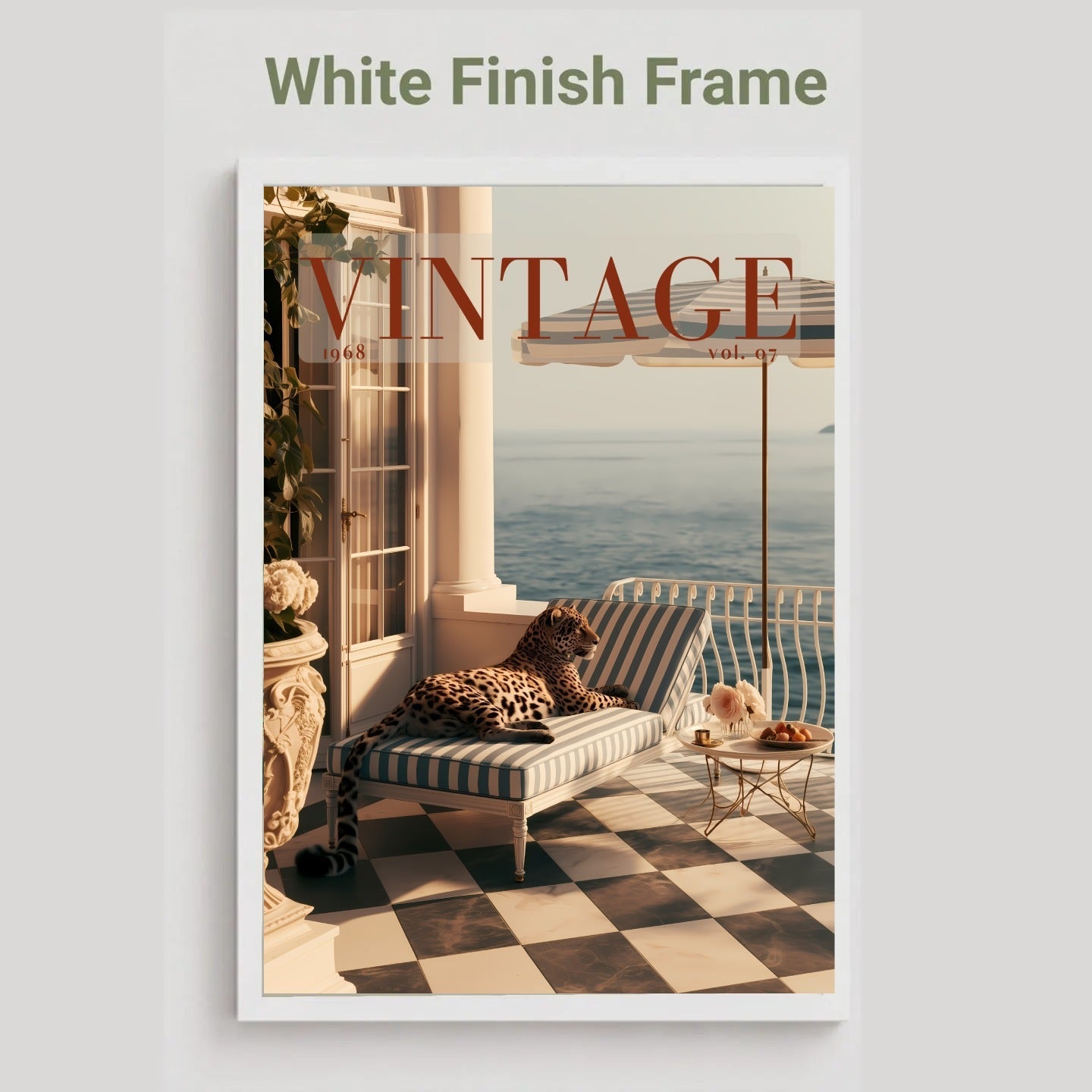A framed vintage-style magazine cover print with the text 'White Finish Frame' above it. The artwork shows a striped lounge chair on a checkered terrace overlooking water, with a leopard resting on the chair and large 'VINTAGE' lettering across the top.