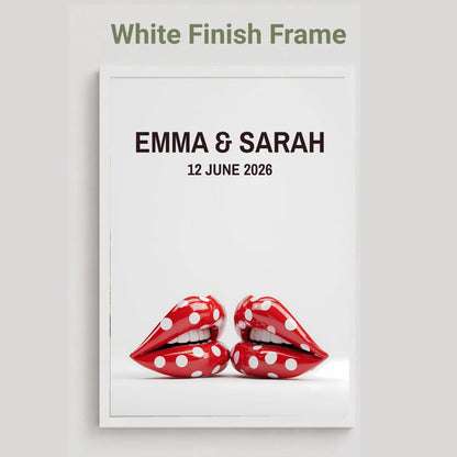 A framed custom wedding print with a white finish frame, featuring the text 'EMMA & SARAH' and '12 JUNE 2026' above a graphic of two red lips with white polka dots, on a light gray background.