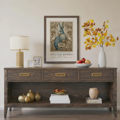 Wooden console table with decorative items including a lamp, framed artwork, and vases. William Morris inspired exhibition poster.