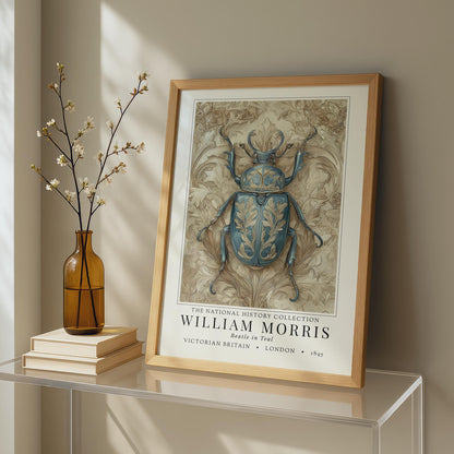 Framed artwork of a beetle with 'William Morris' text on a shelf with a vase and books.William Morris teal beetle exhibition print in a black frame on a cream painted wall, victorian insect art poster