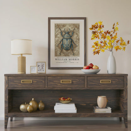 Wooden console table with decorative items including a lamp, framed artwork, and vases.William Morris teal beetle exhibition print in a black frame on a cream painted wall, victorian insect art poster