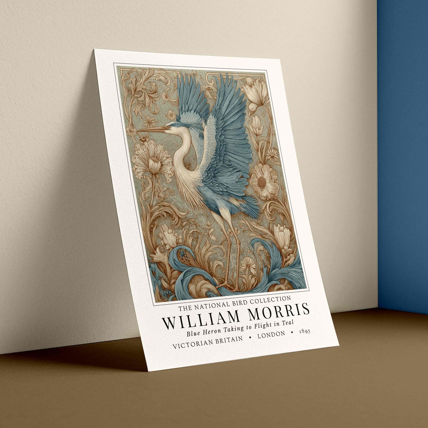 Decorative poster with a bird design leaning against a wall. William Morris style exhibition poster featuring a blue heron taking to flight, surrounded by ornate acanthus scrolls, dahlias and botanical foliage in teal, gold and antique cream — Arts & Crafts wall art print