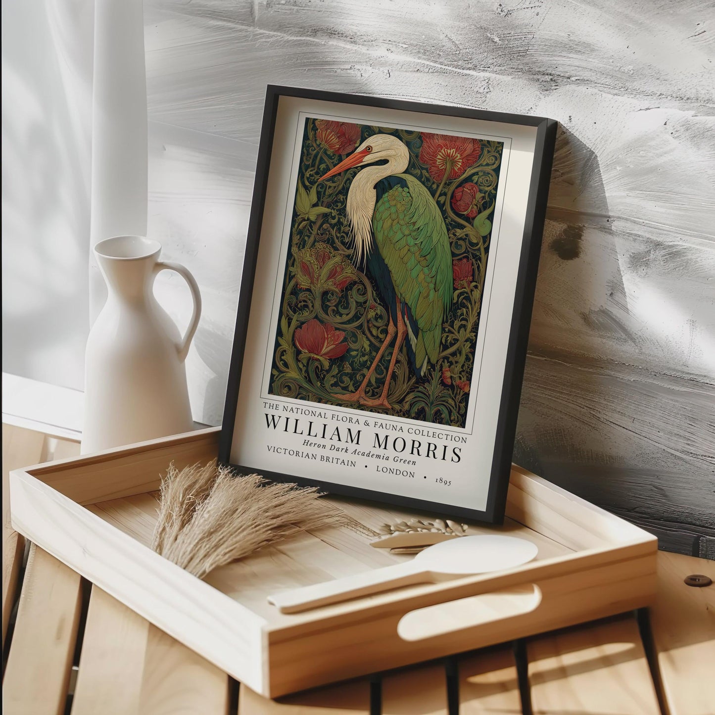 Framed William Morris print on a wooden tray with decorative items. William Morris inspired heron exhibition poster in a jewel-toned palette of forest green, antique crimson and old gold, featuring a grey heron amid ornate pimpernel blooms and curling vines — Victorian Arts and Crafts style, framed print.