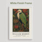 Black framed artwork of a William Morris inspired heron exhibition poster in a jewel-toned palette of forest green, antique crimson and old gold, featuring a grey heron amid ornate pimpernel blooms and curling vines — Victorian Arts and Crafts style, framed print.