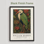Black framed artwork of a William Morris inspired heron exhibition poster in a jewel-toned palette of forest green, antique crimson and old gold, featuring a grey heron amid ornate pimpernel blooms and curling vines — Victorian Arts and Crafts style, framed print.