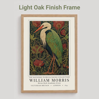 Black framed artwork of a William Morris inspired heron exhibition poster in a jewel-toned palette of forest green, antique crimson and old gold, featuring a grey heron amid ornate pimpernel blooms and curling vines — Victorian Arts and Crafts style, framed print.