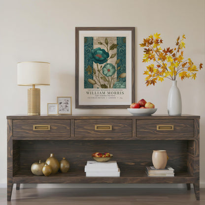Wooden console table with decorative items including a lamp, framed artwork, and vases. A framed botanical print showcasing teal flowers with red centers and green foliage. The print is from the William Morris collection, with text indicating "Victorian Britain" and "London 1895". The artwork has a vintage style.