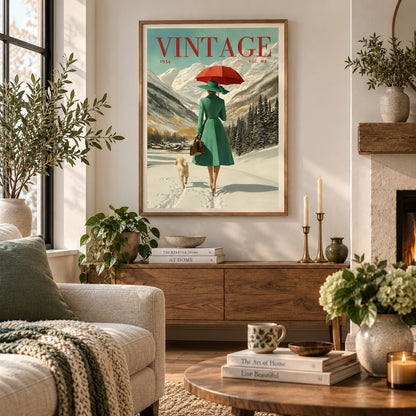 A framed vintage-style wall art print hangs above a wooden console in a styled living room. The artwork shows a woman in a green coat and red umbrella walking through snow with mountains in the background and the word 'VINTAGE' at the top.