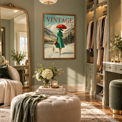 A framed vintage-style wall art print hangs in a styled dressing room. The print shows a woman in a green coat walking in the snow with a red umbrella, and the word VINTAGE appears at the top.
